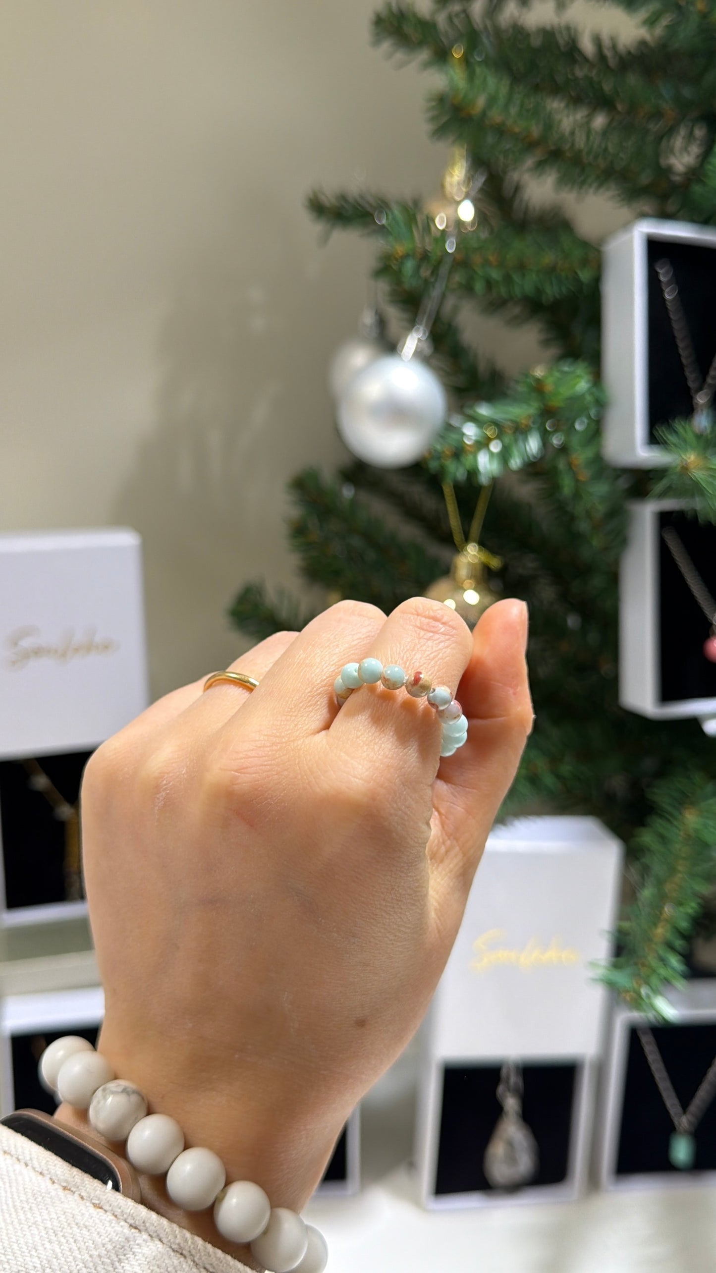 Hand wearing a bracelet with a Christmas tree and decorations in the background