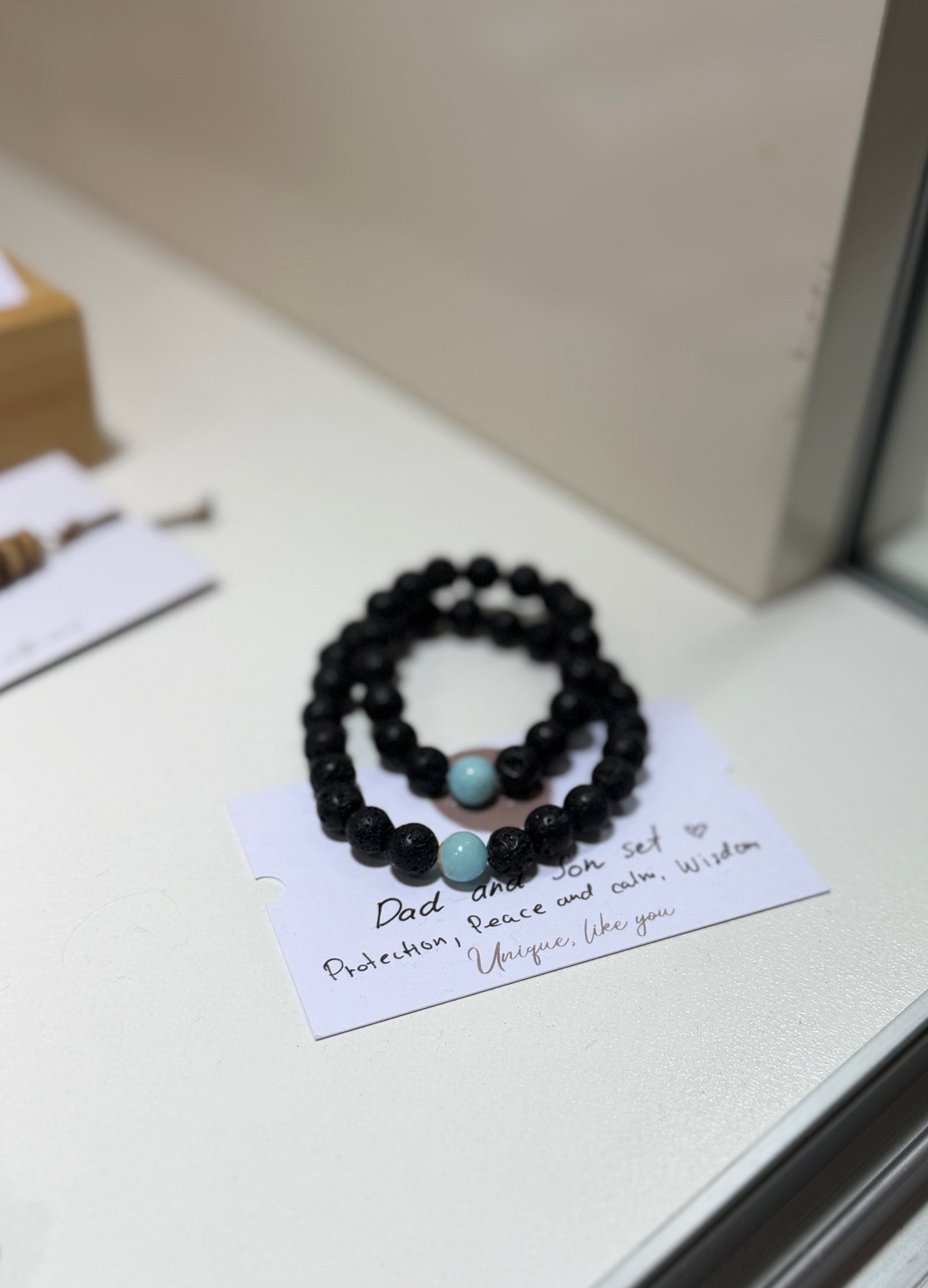 Black beaded bracelets with turquoise stones on a card with text, placed on a light surface.
