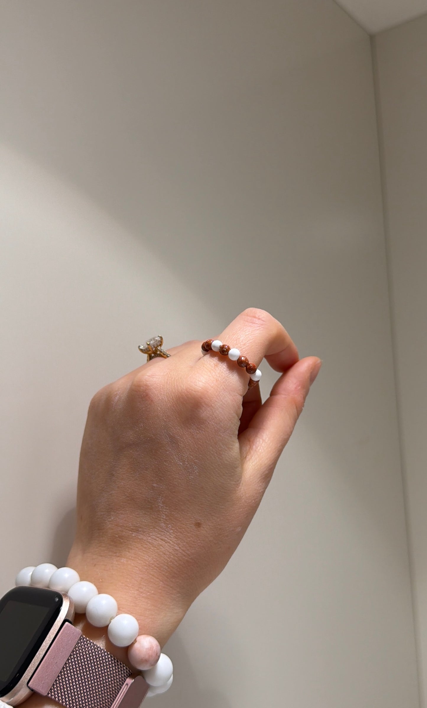 Hand wearing a bracelet and ring against a neutral background