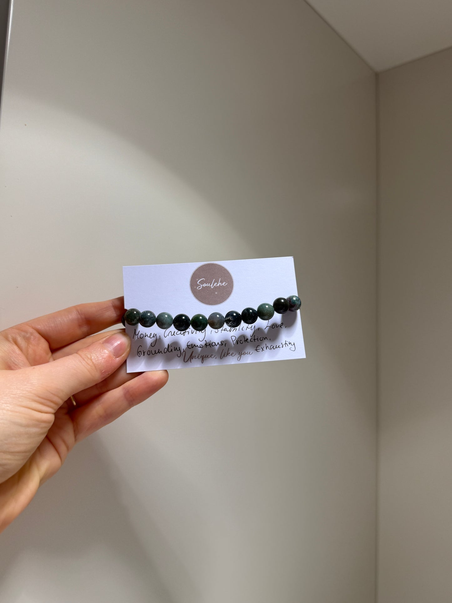 Hand holding a card with a bracelet on a plain background