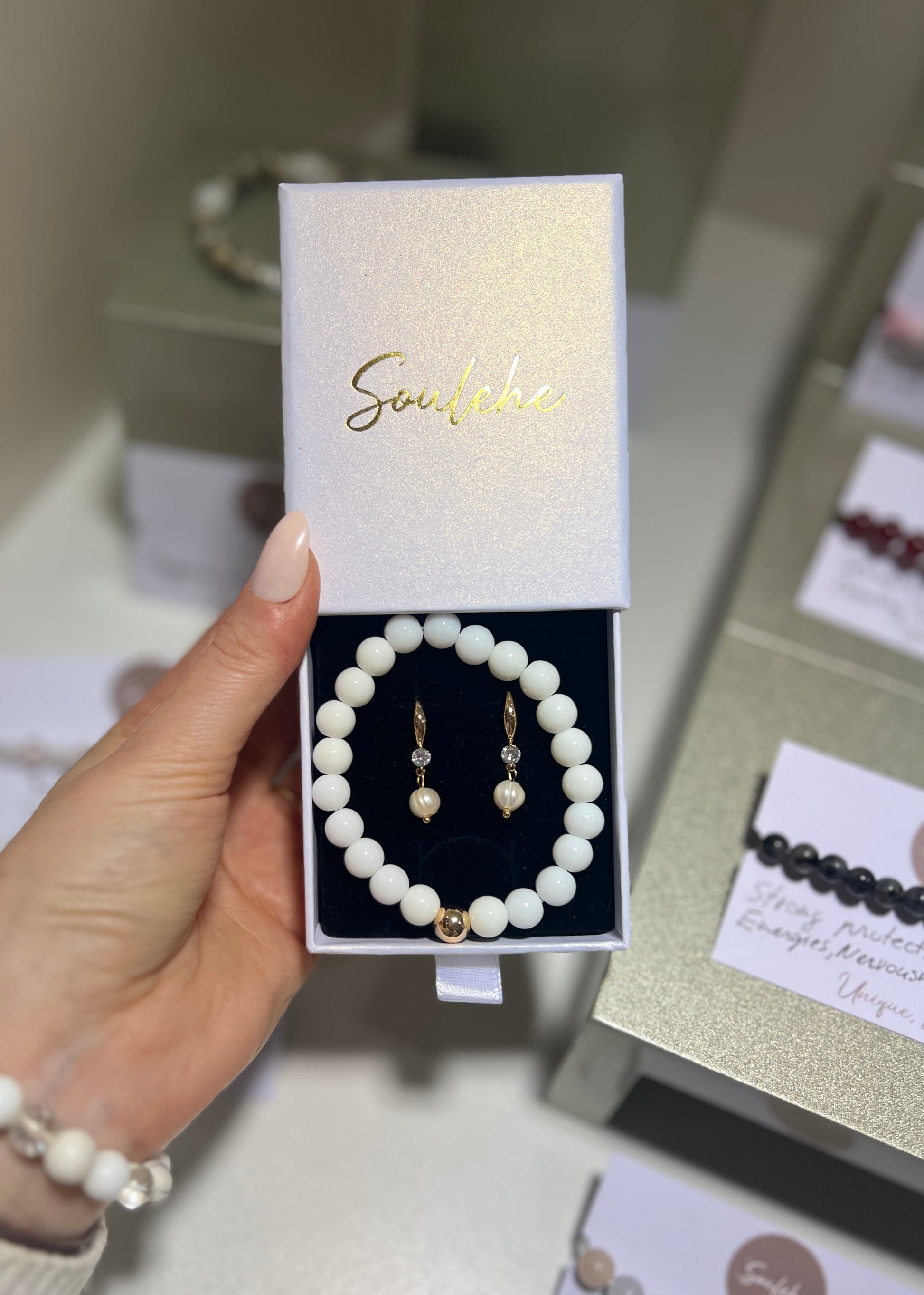 Pearl bracelet and earrings set in a branded box held by a hand.