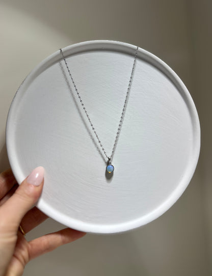 Necklace with a pendant on a white plate held by a hand against a neutral background
