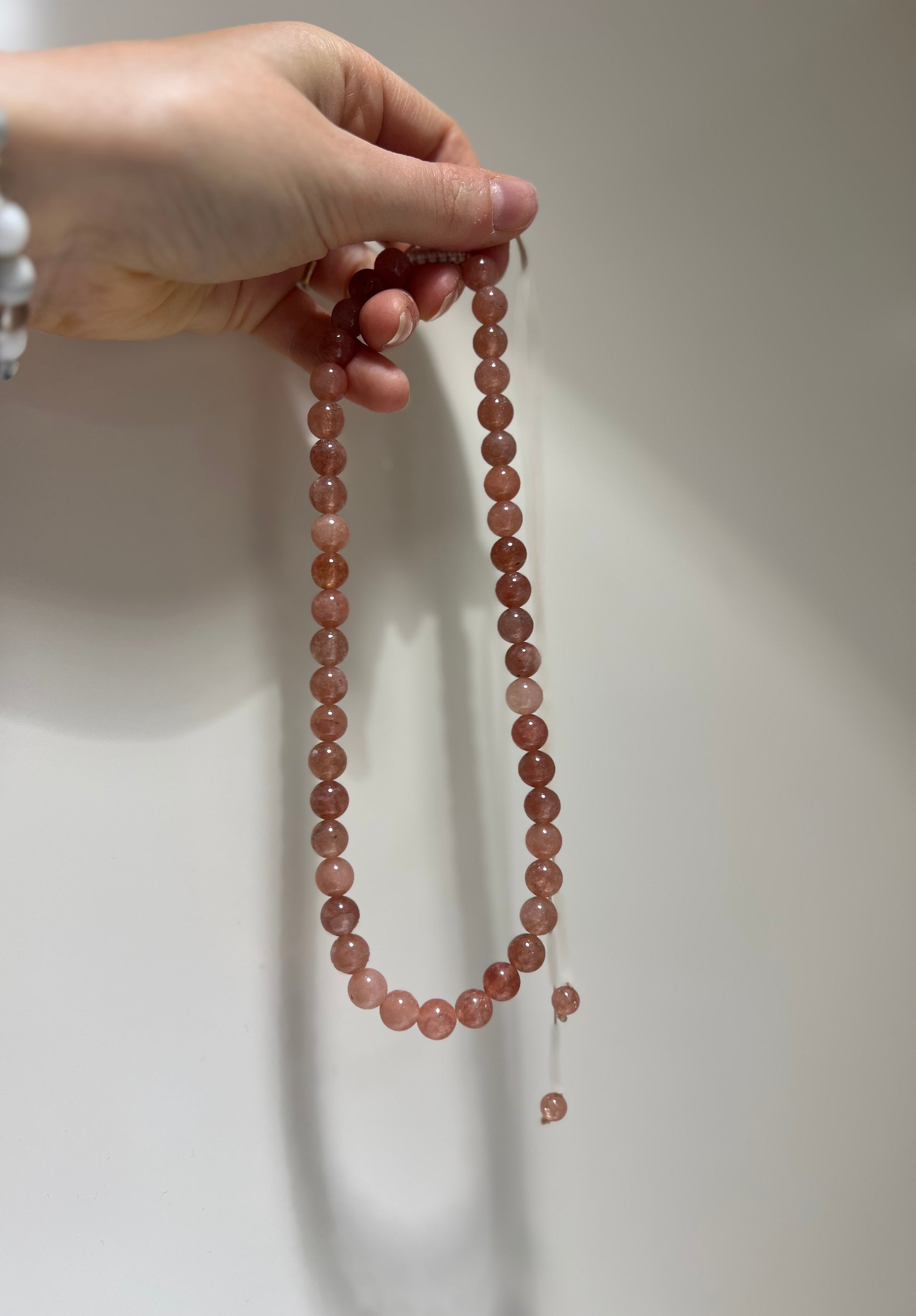 Hand holding a string of pink beads against a neutral background