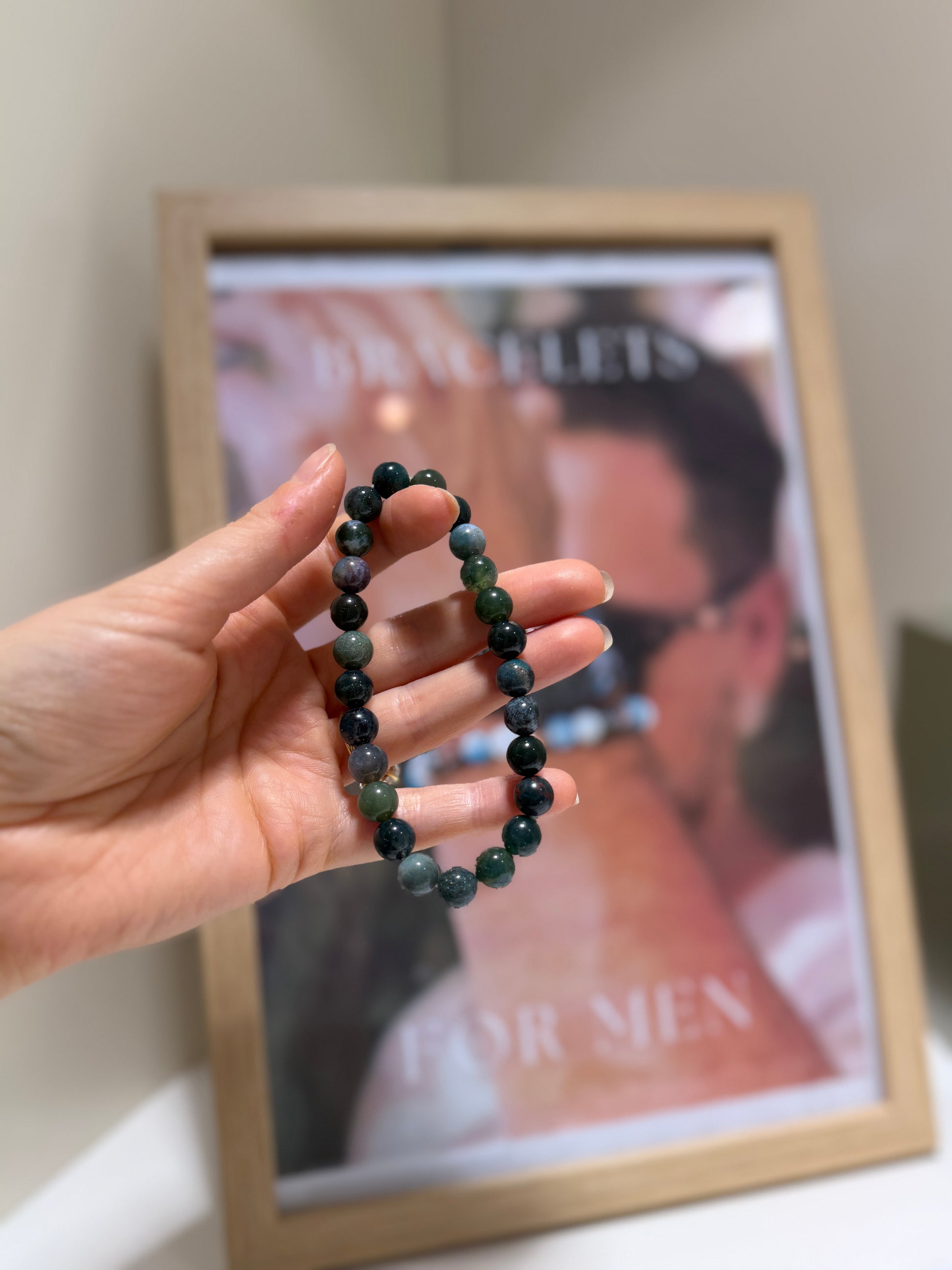 Hand holding a beaded bracelet in front of a framed picture