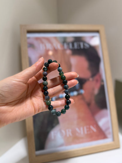 Hand holding a beaded bracelet in front of a framed picture