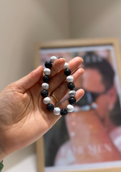 Hand holding a black, white, and gray beaded bracelet with a blurred background
