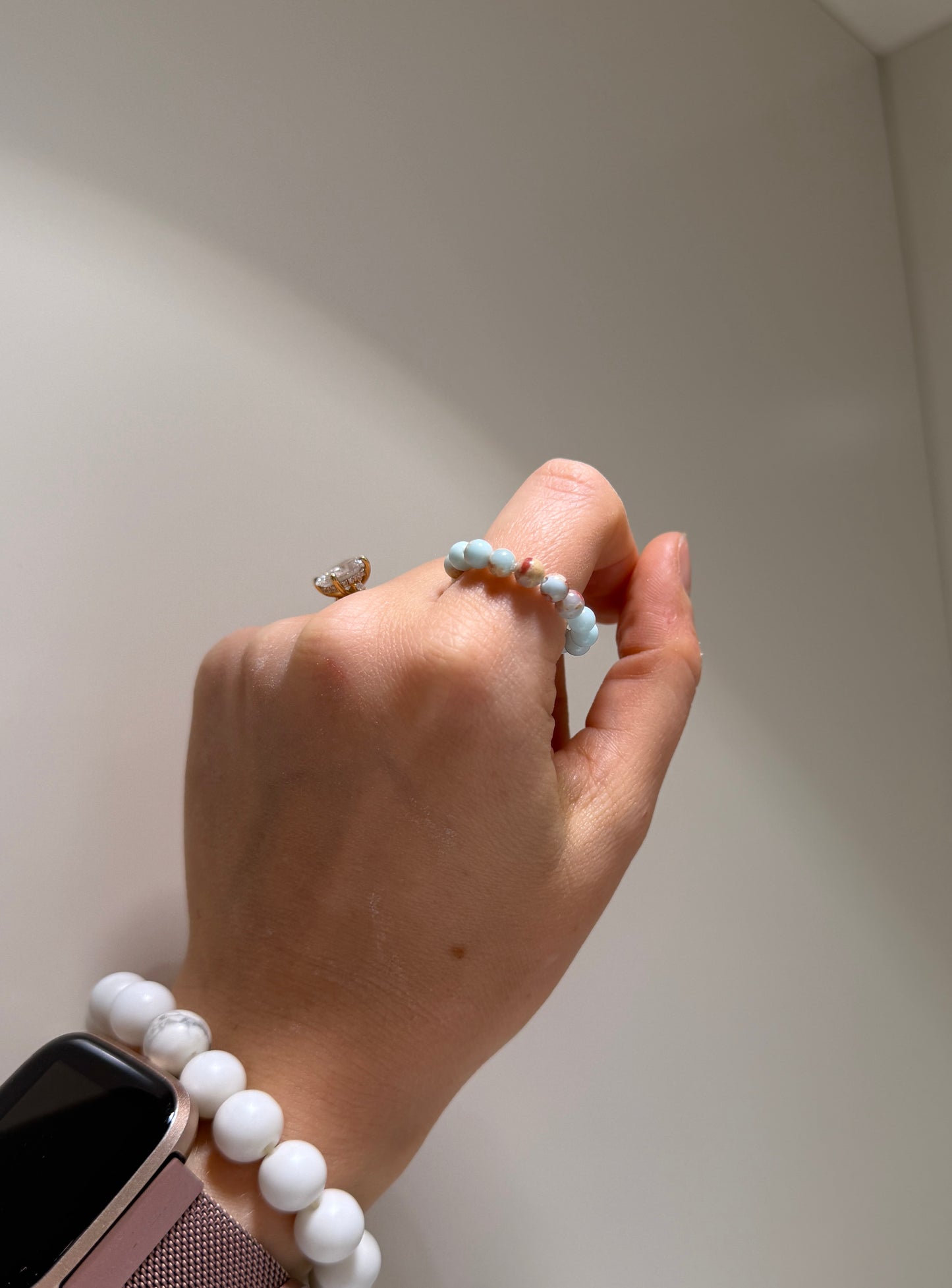 Hand wearing a white beaded bracelet with a plain background