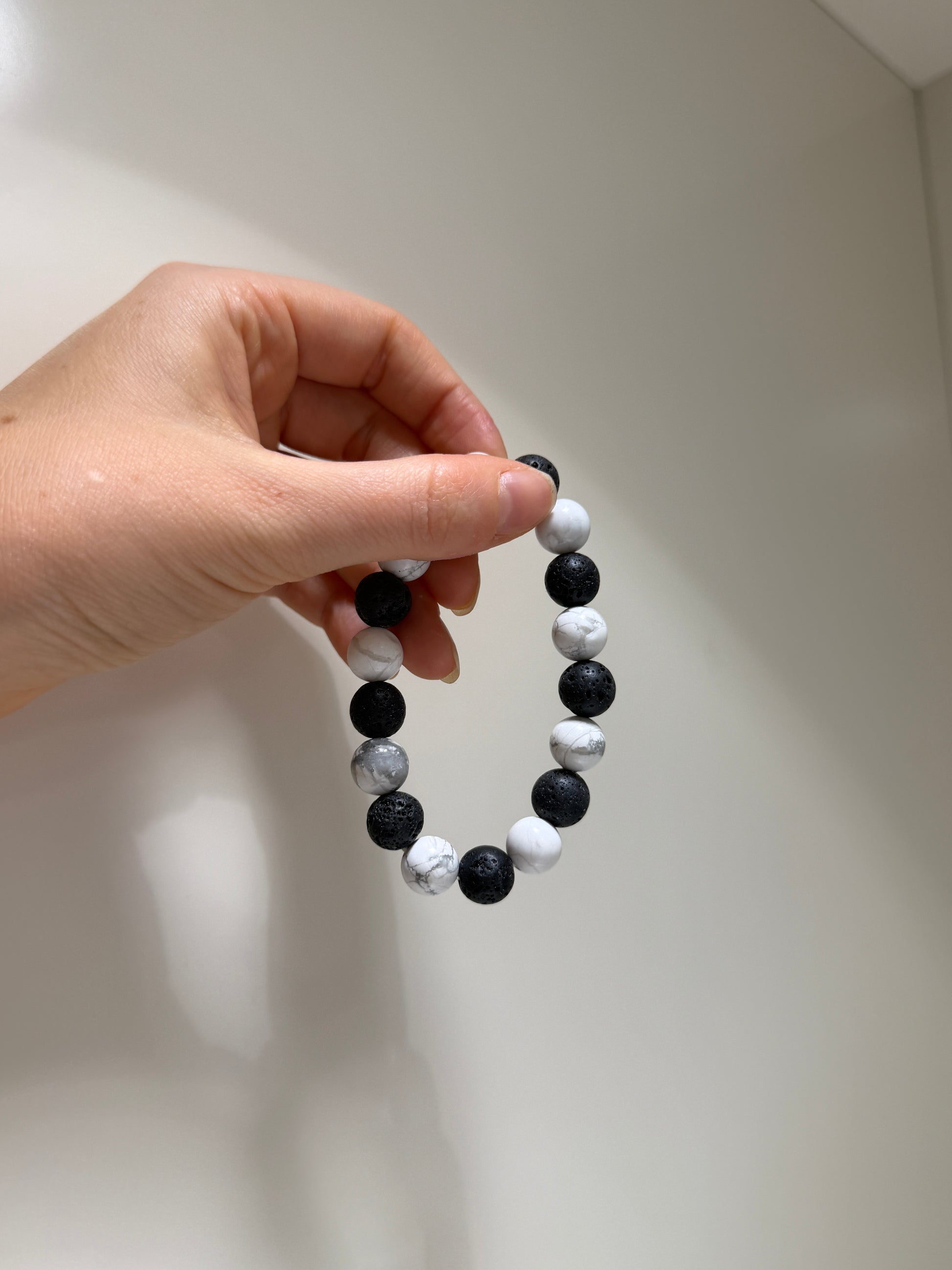 Hand holding a black and white beaded bracelet against a neutral background