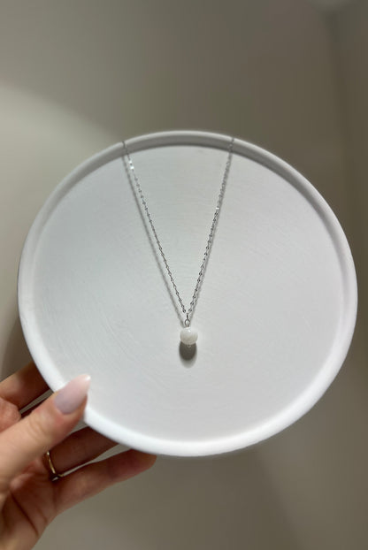 Silver necklace on a white circular stand held by a hand against a neutral background