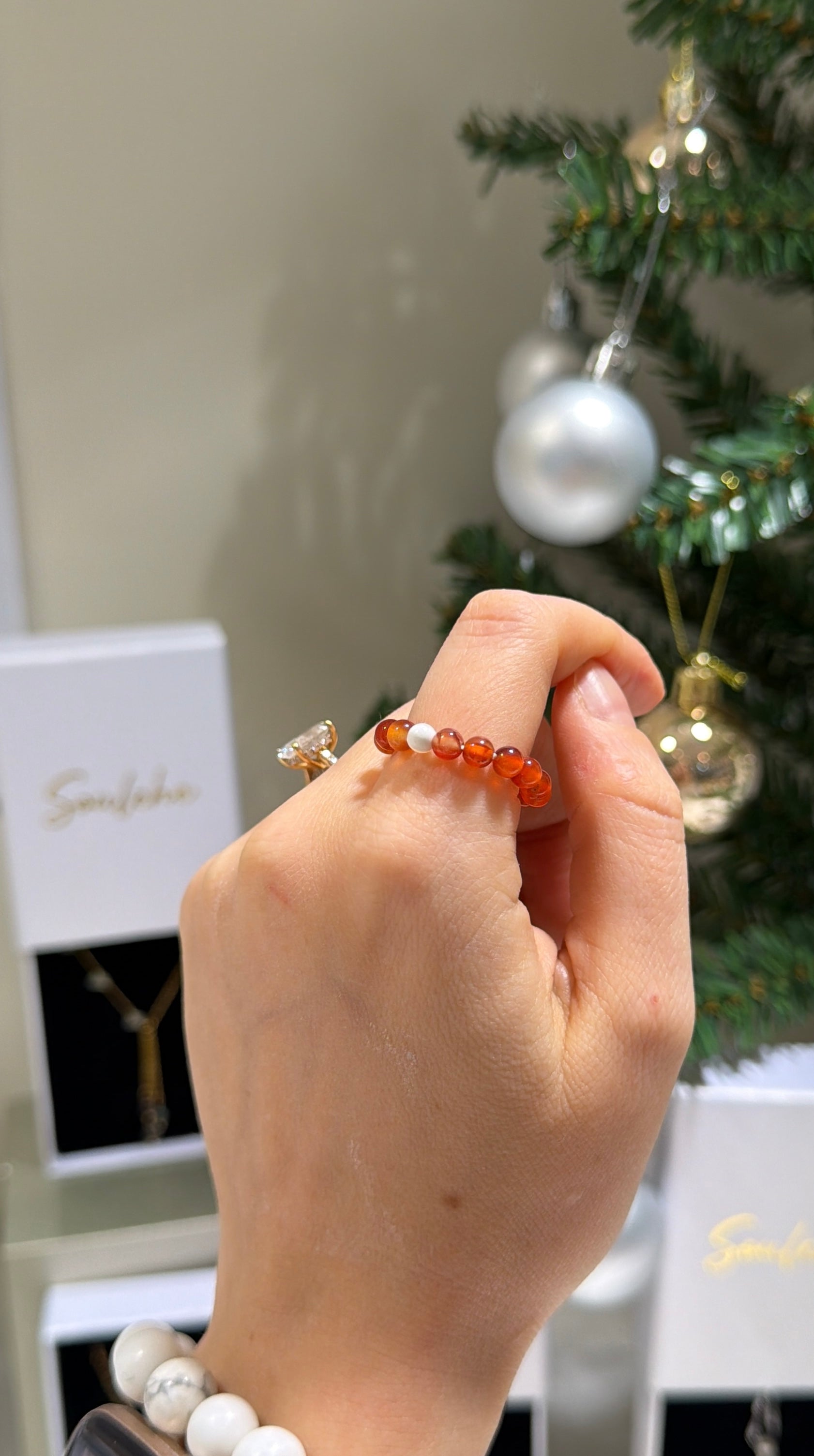 Hand wearing a beaded ring with a Christmas tree in the background