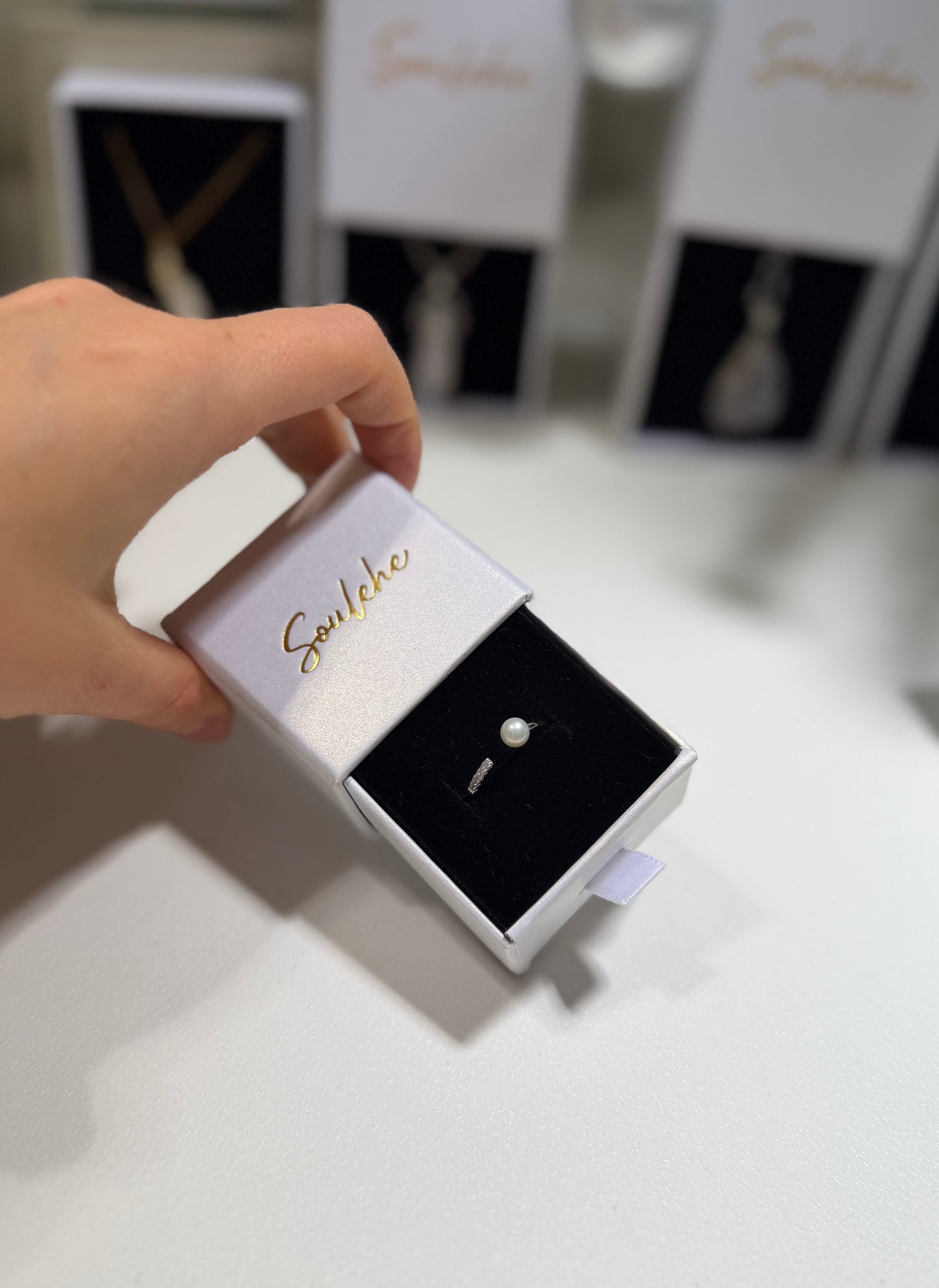 Hand holding a small box with a diamond ring inside, branded 'Soulehe'.