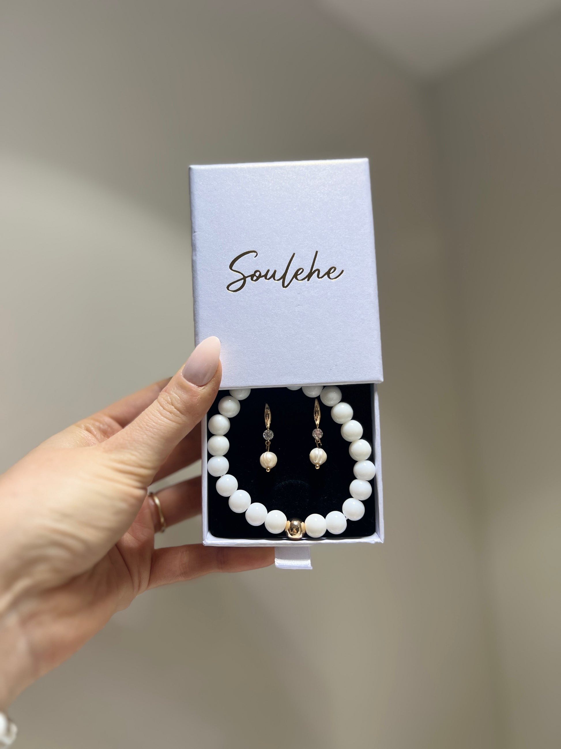 Pearl necklace and earrings set in a 'Soulehe' box held by a hand.