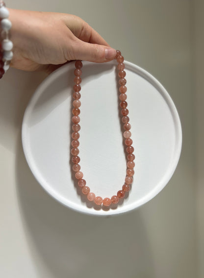 Necklace with pink beads on a white plate held by a hand against a neutral background