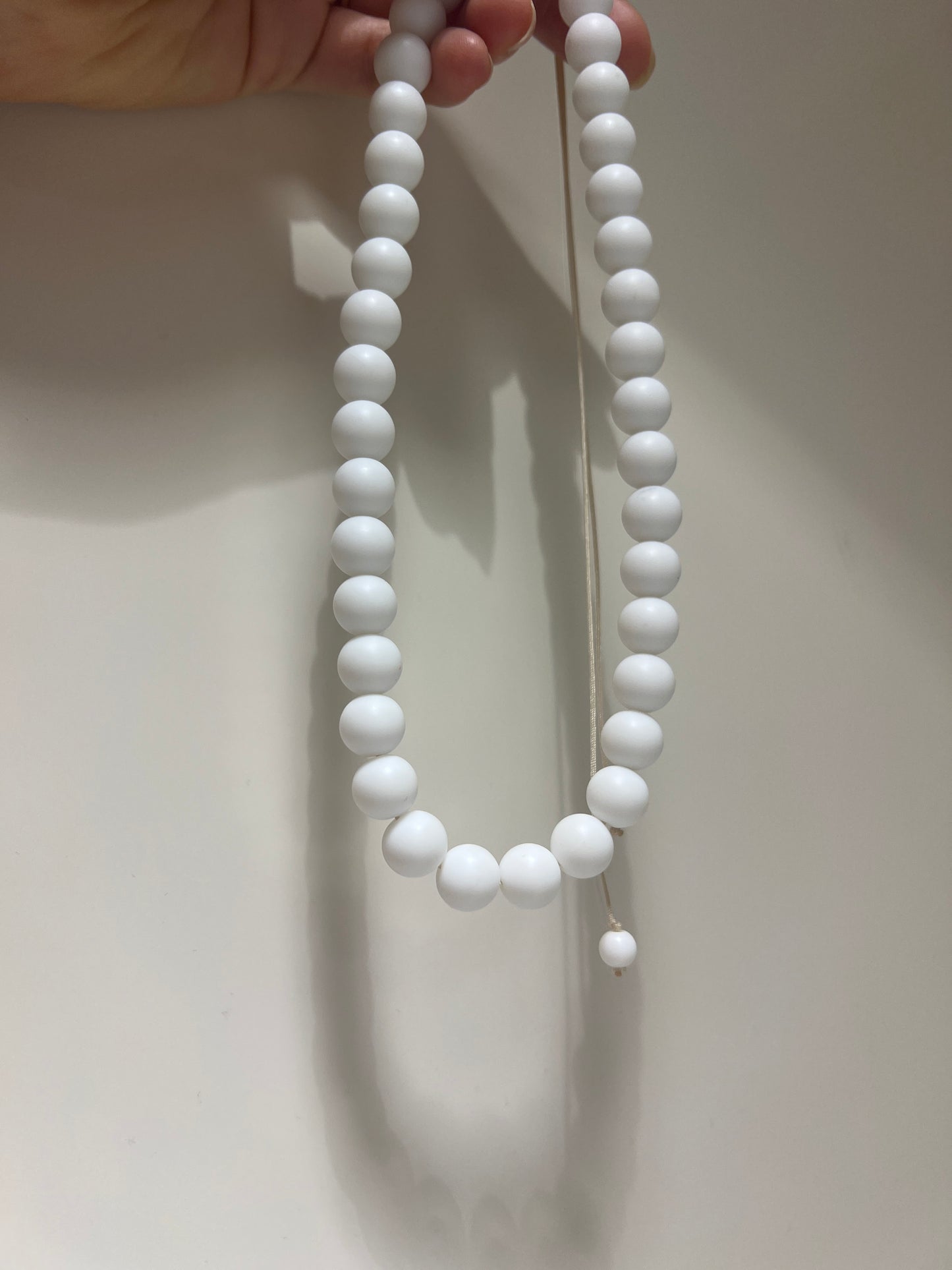 White beaded necklace held by a hand against a light background