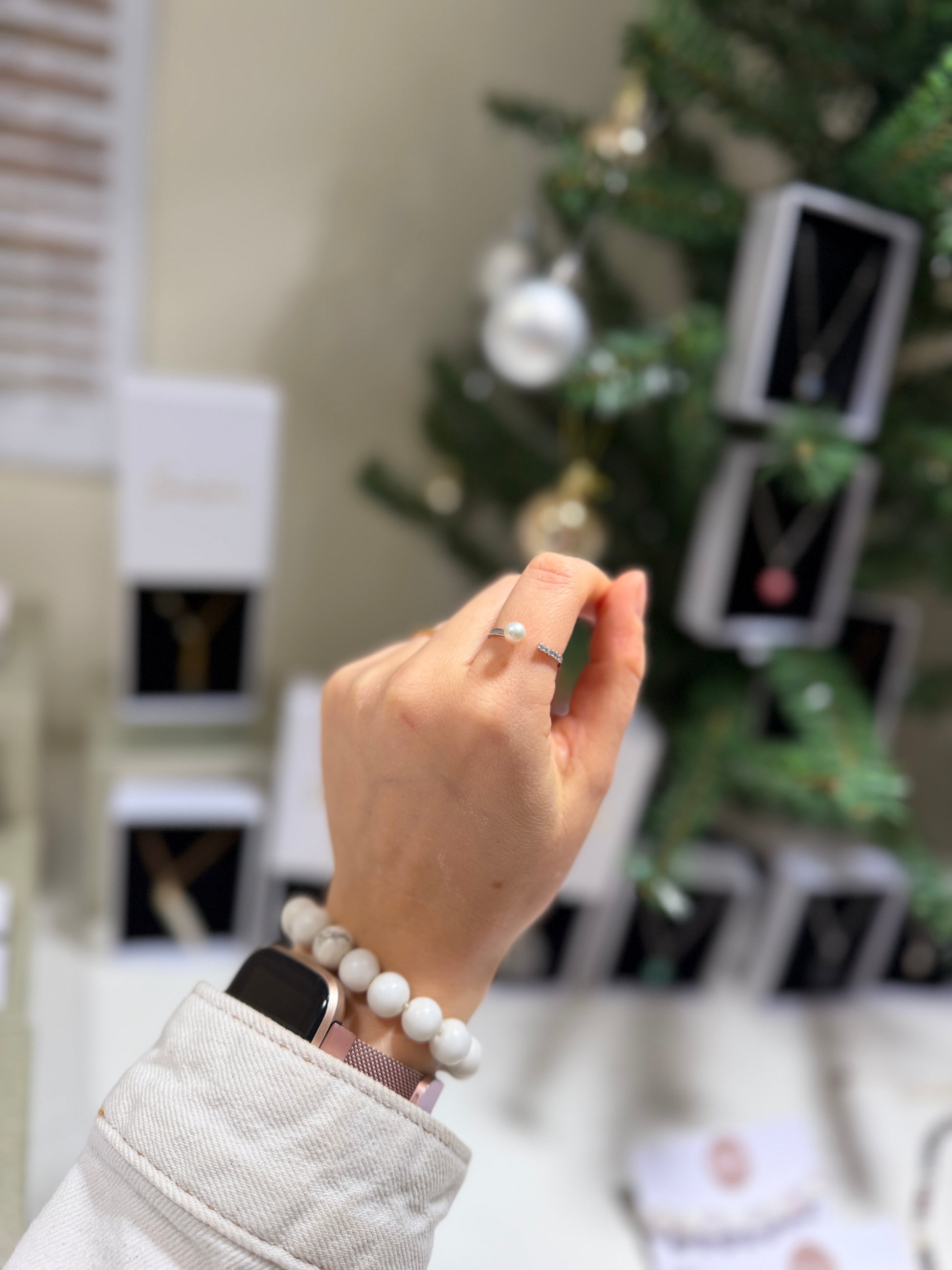 Hand with a ring and bracelet in front of a decorated Christmas tree.