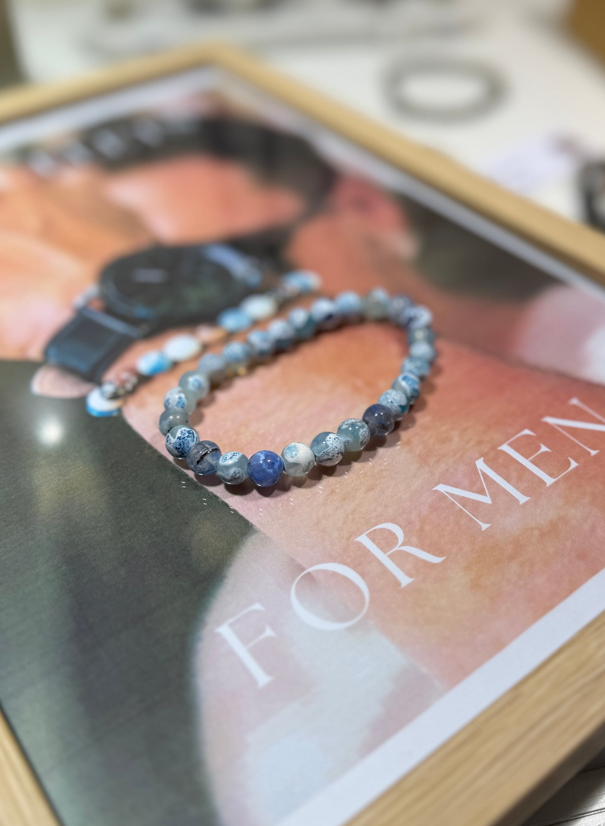Blue beaded bracelet on a man's wrist with a magazine in the background