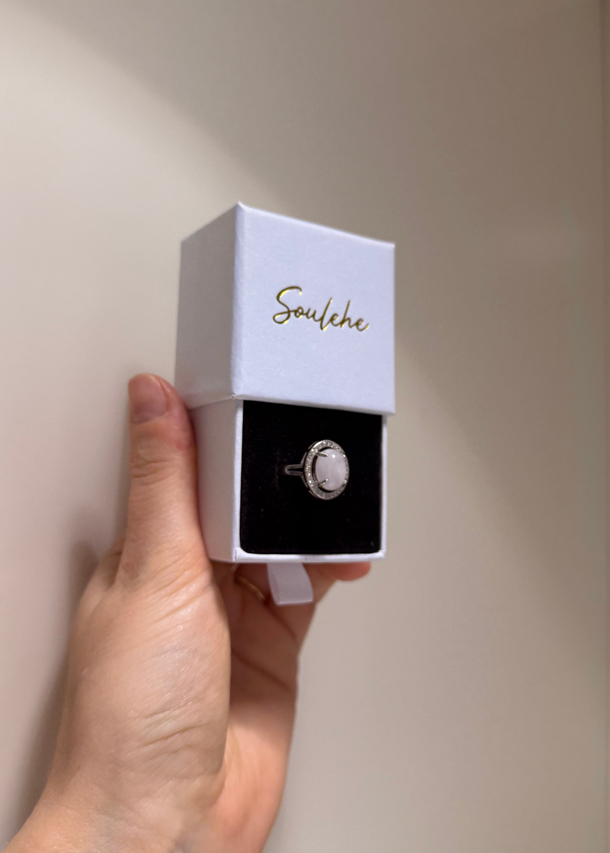 Hand holding a white jewelry box with a ring inside, branded 'Soulehe'.