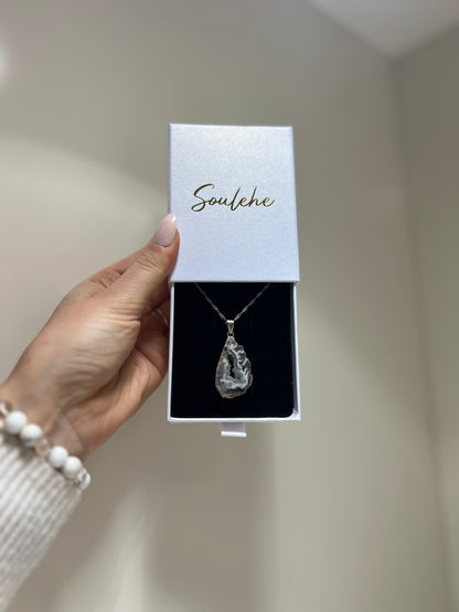 Hand holding a necklace in a 'Soulehe' box against a neutral background