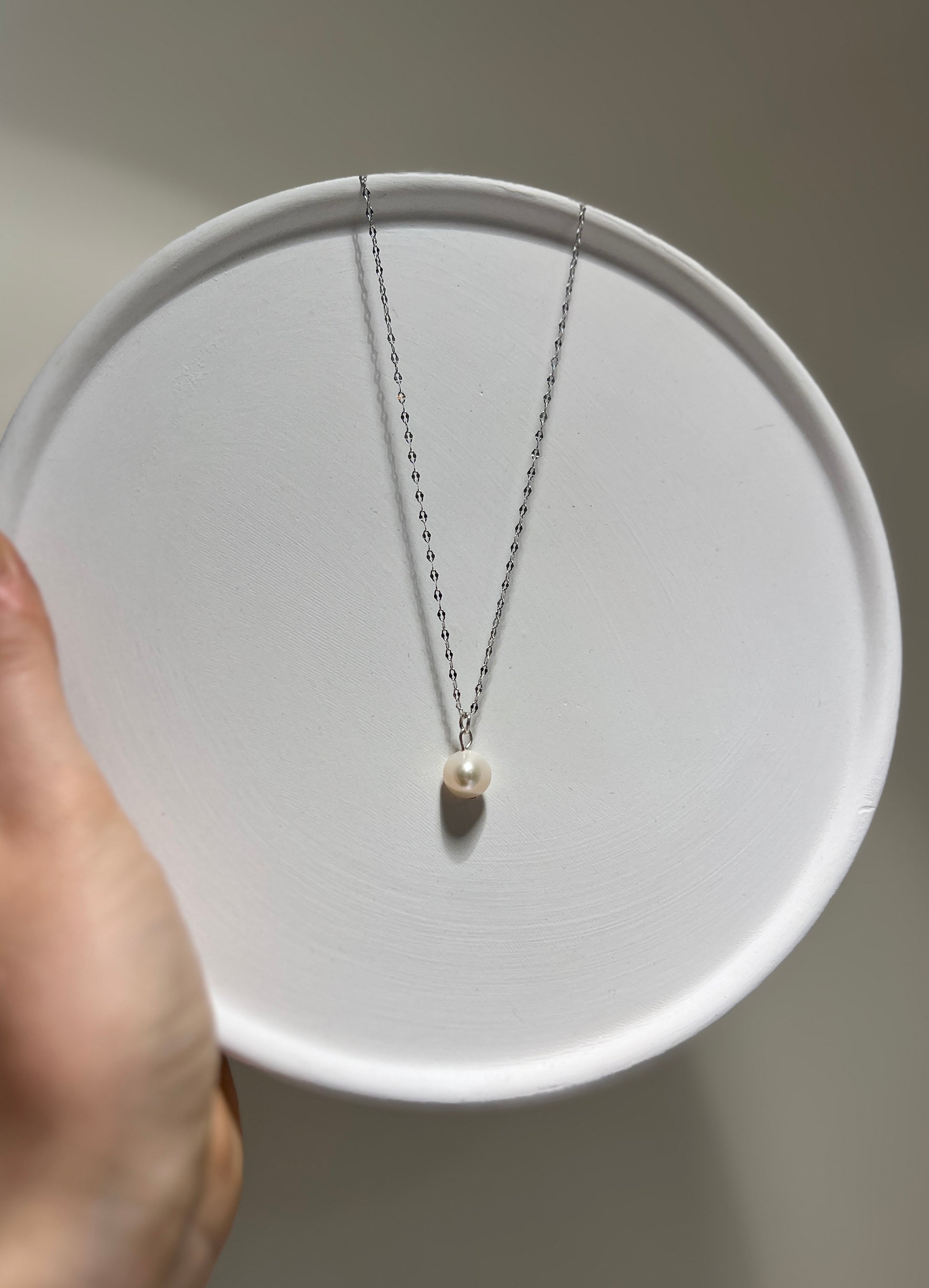 Pearl necklace on a white plate held by a hand