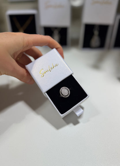 Jewelry box with a ring inside, held by a hand on a light surface.