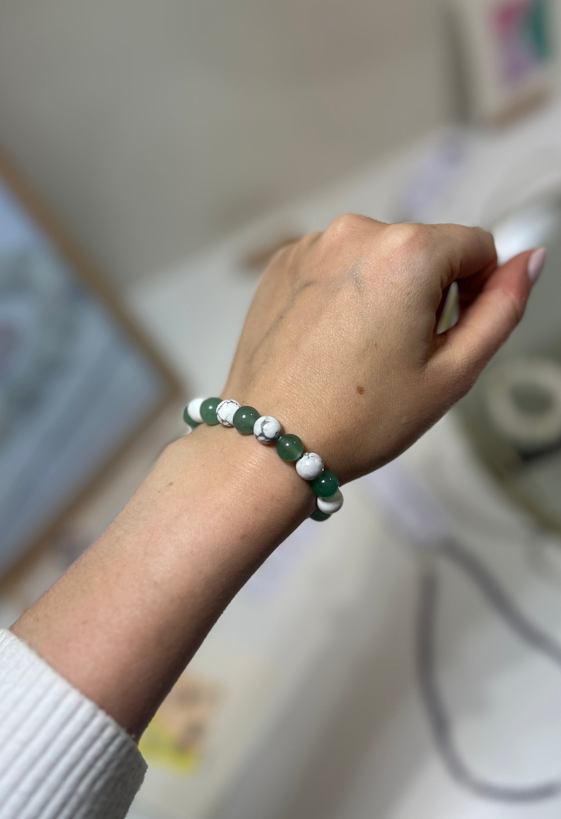 Hand wearing a bracelet with green and white beads on a blurred background