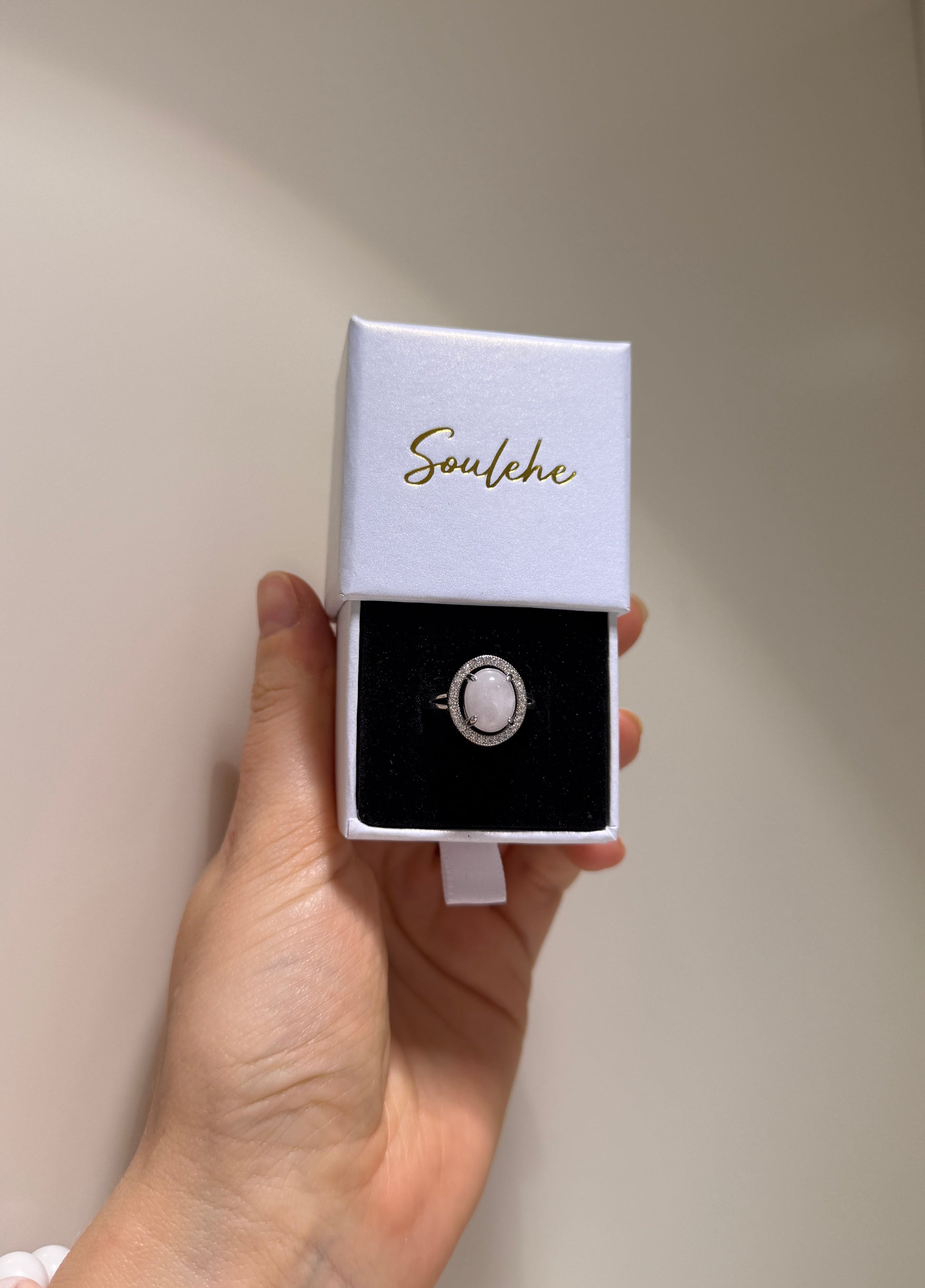 Hand holding a ring in a 'Soulehe' box against a plain background