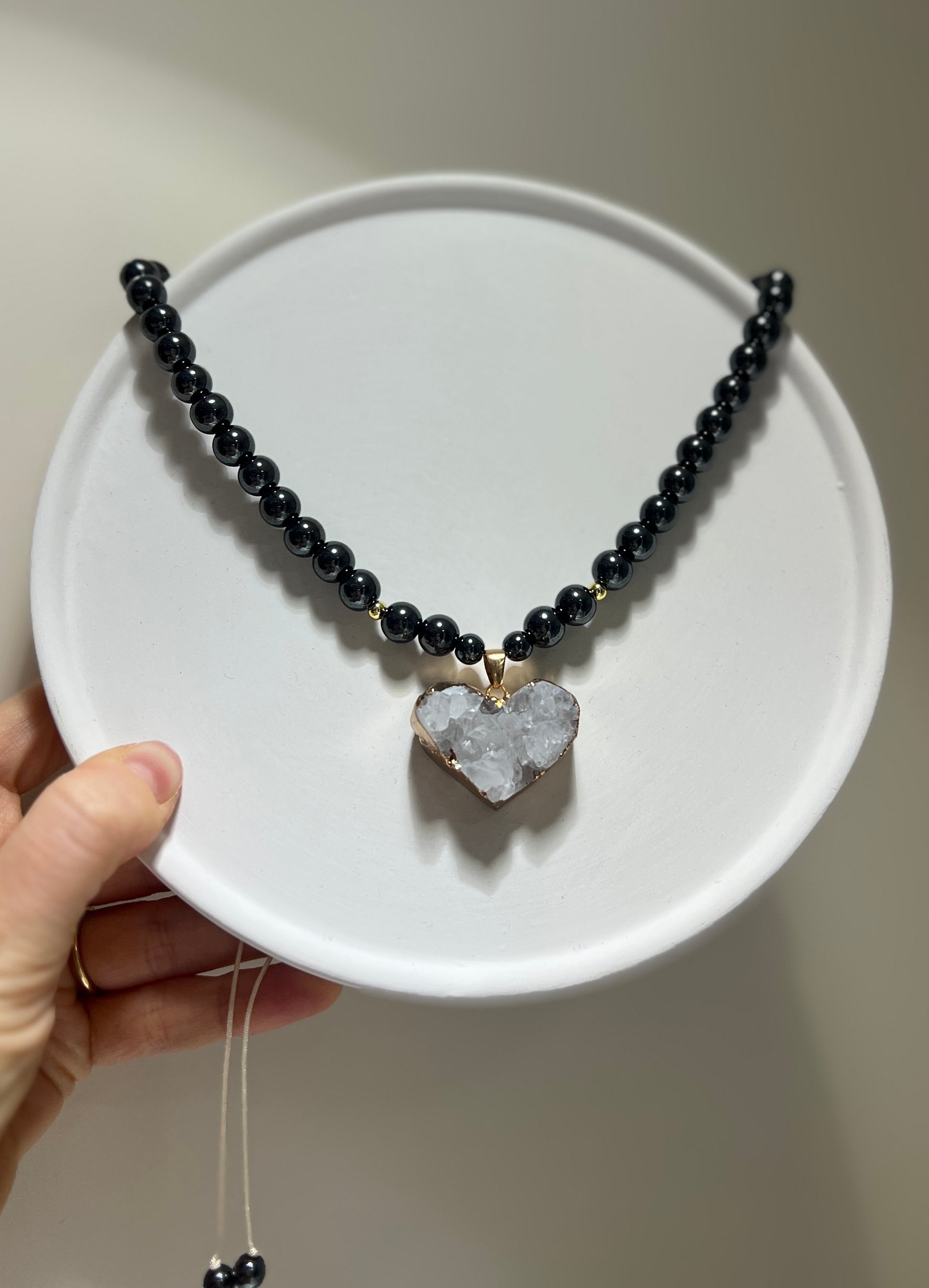 Necklace with black beads and a heart-shaped crystal pendant on a white plate.