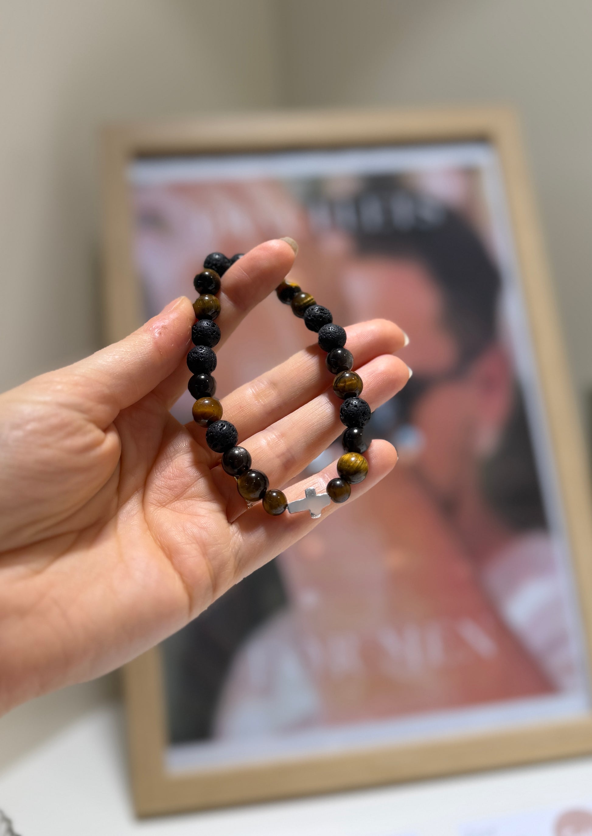 Hand holding a beaded bracelet in front of a blurred photo frame