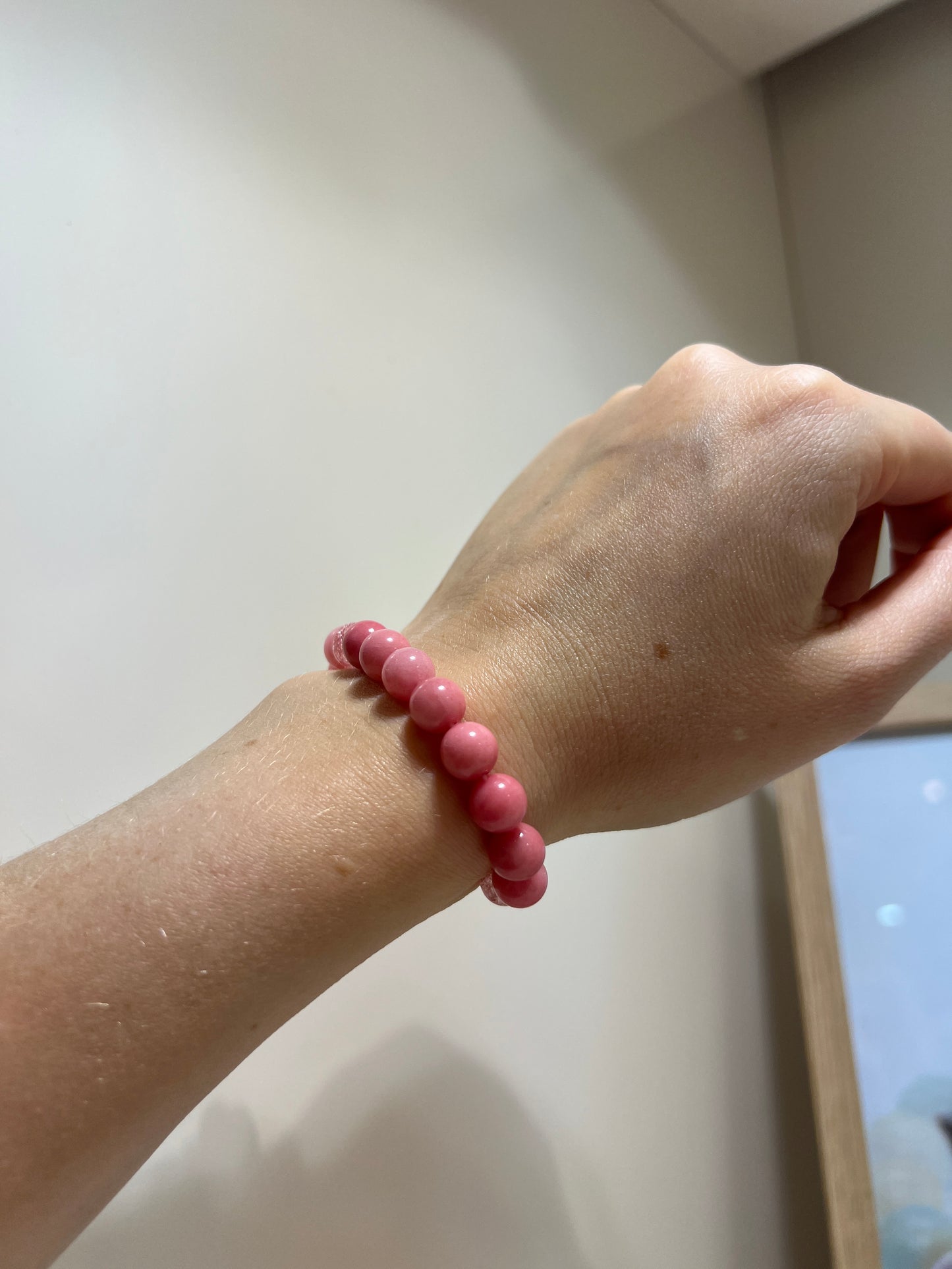 Hand wearing a pink beaded bracelet on a light background