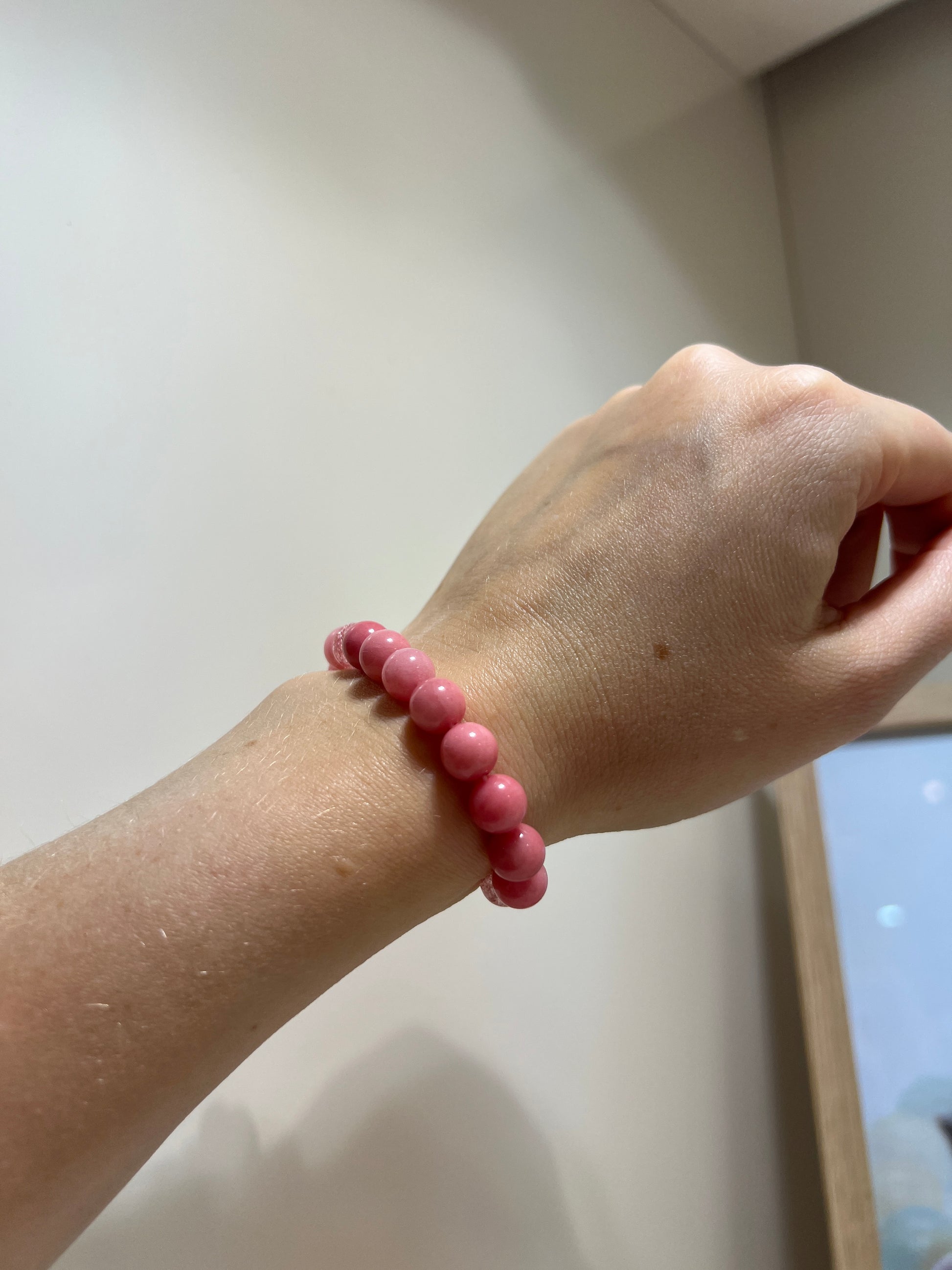 Hand wearing a pink beaded bracelet on a light background