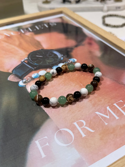 Two beaded bracelets on a magazine with a watch on top