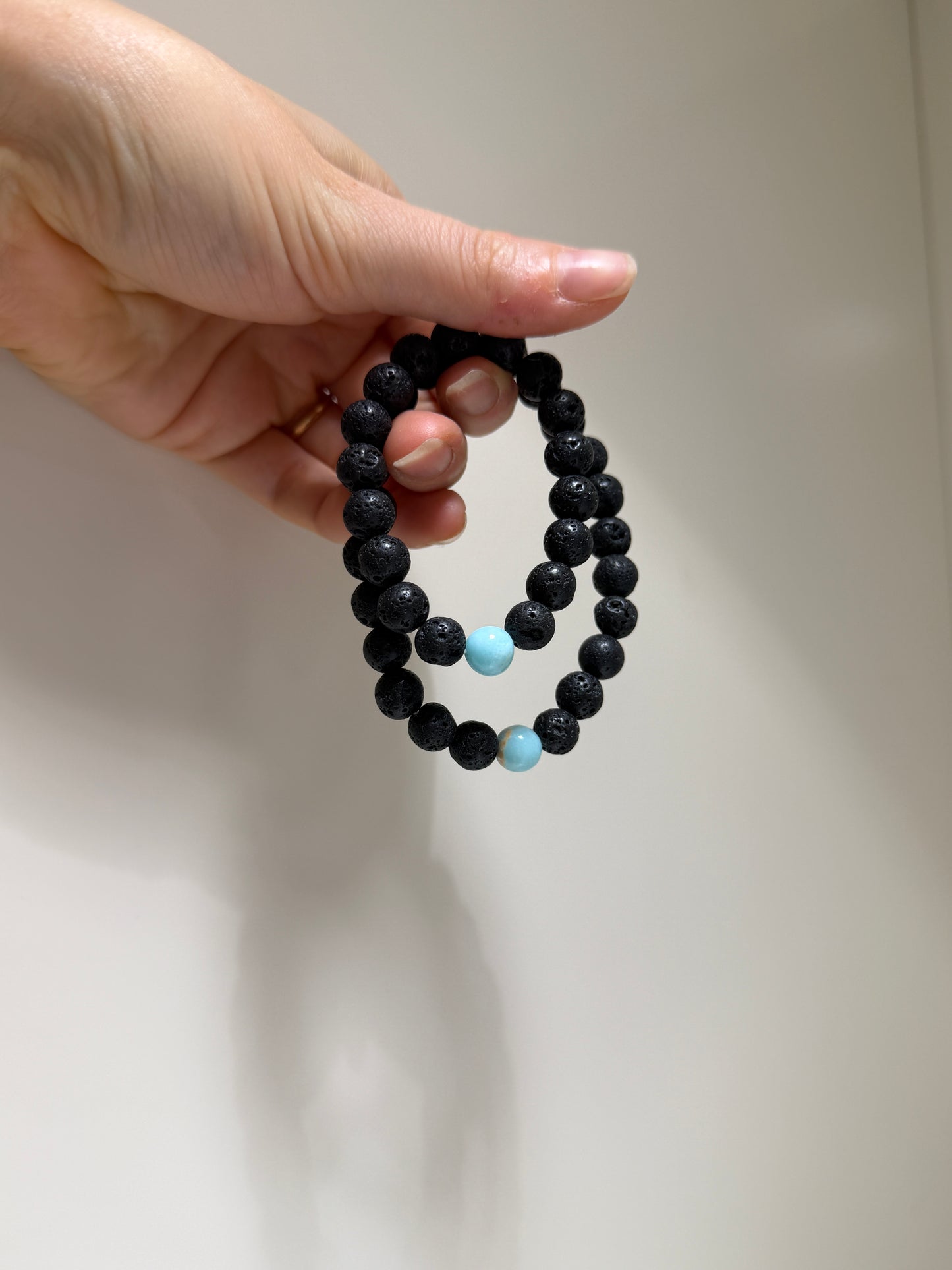 Black beaded bracelet with a blue bead held in a hand against a plain background