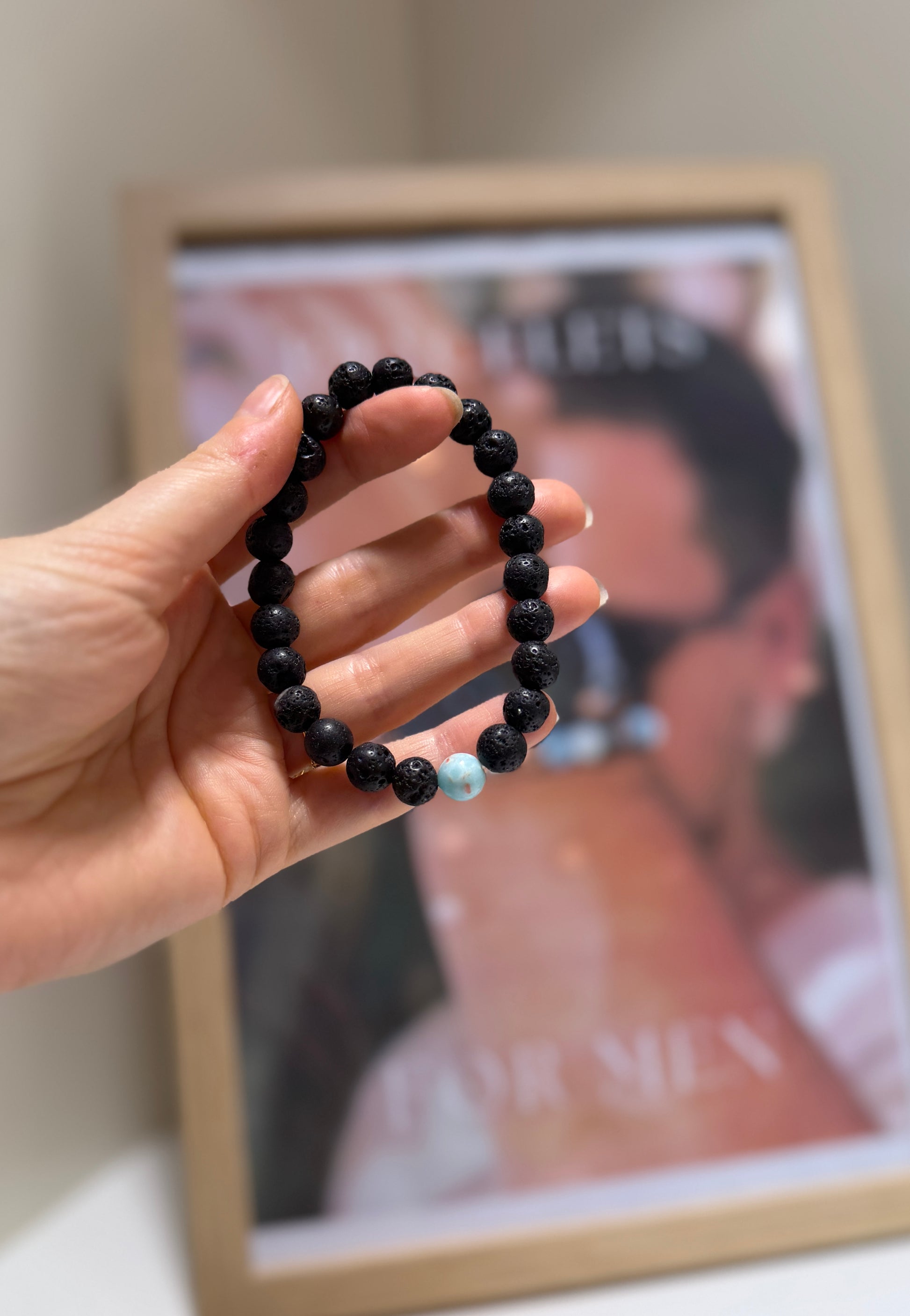 Hand holding a black beaded bracelet in front of a framed picture