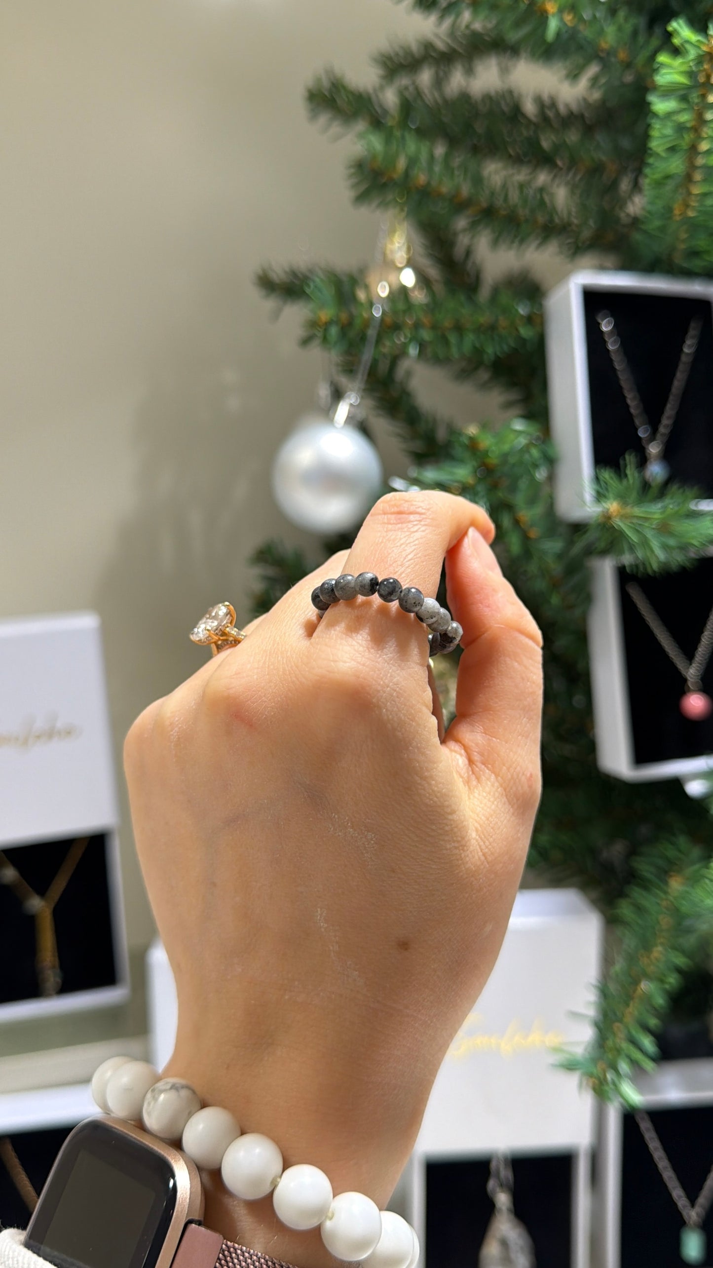 Hand wearing a ring with a Christmas tree and jewelry display in the background