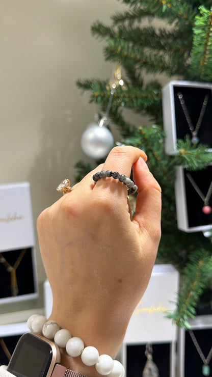 Hand wearing a ring with a Christmas tree and jewelry display in the background