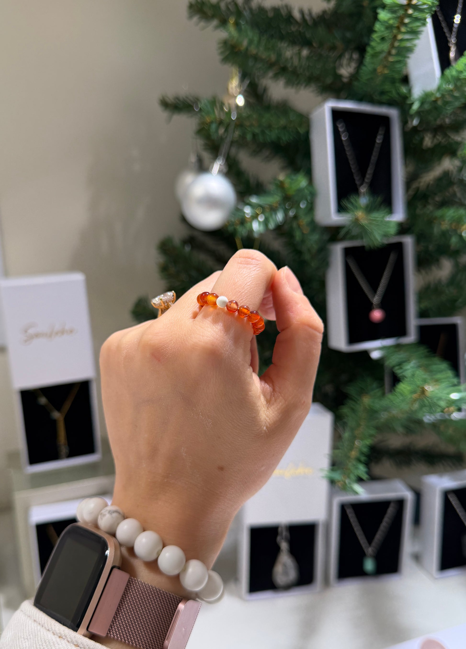 Hand wearing a bracelet with a Christmas tree and jewelry boxes in the background