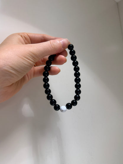 Hand holding a black beaded bracelet against a light background