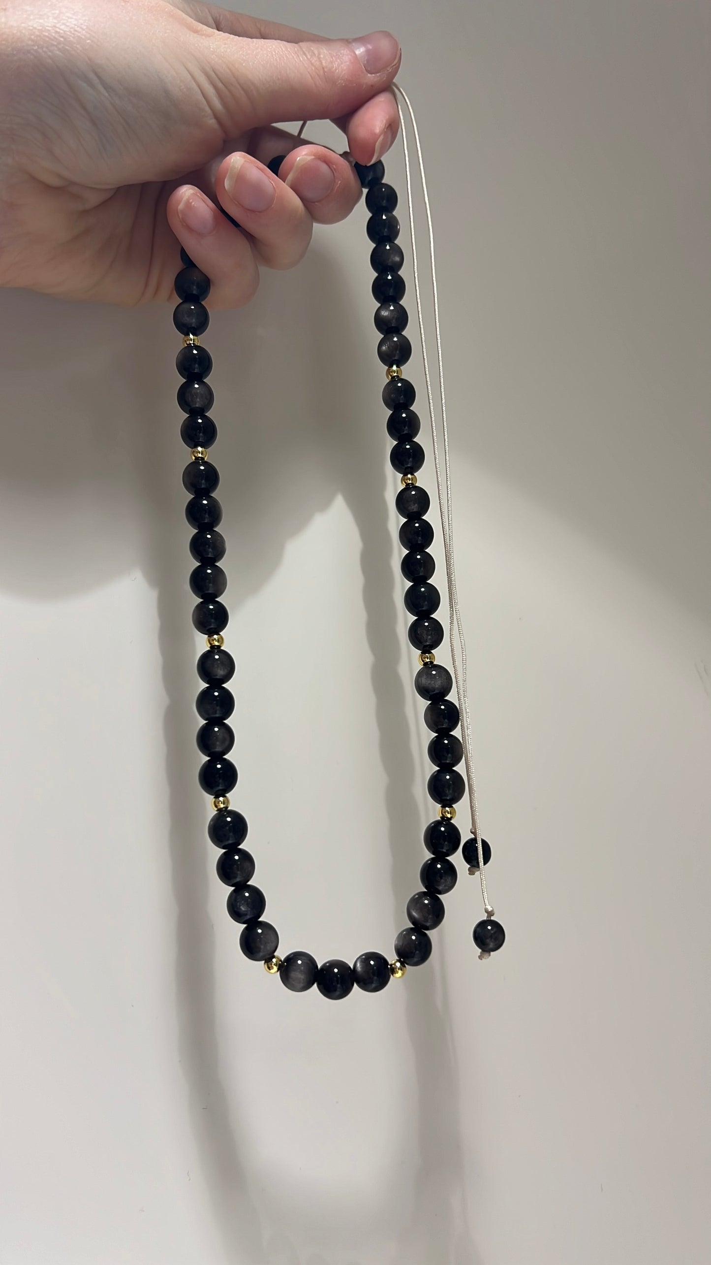 Black beaded necklace held by a hand against a plain background