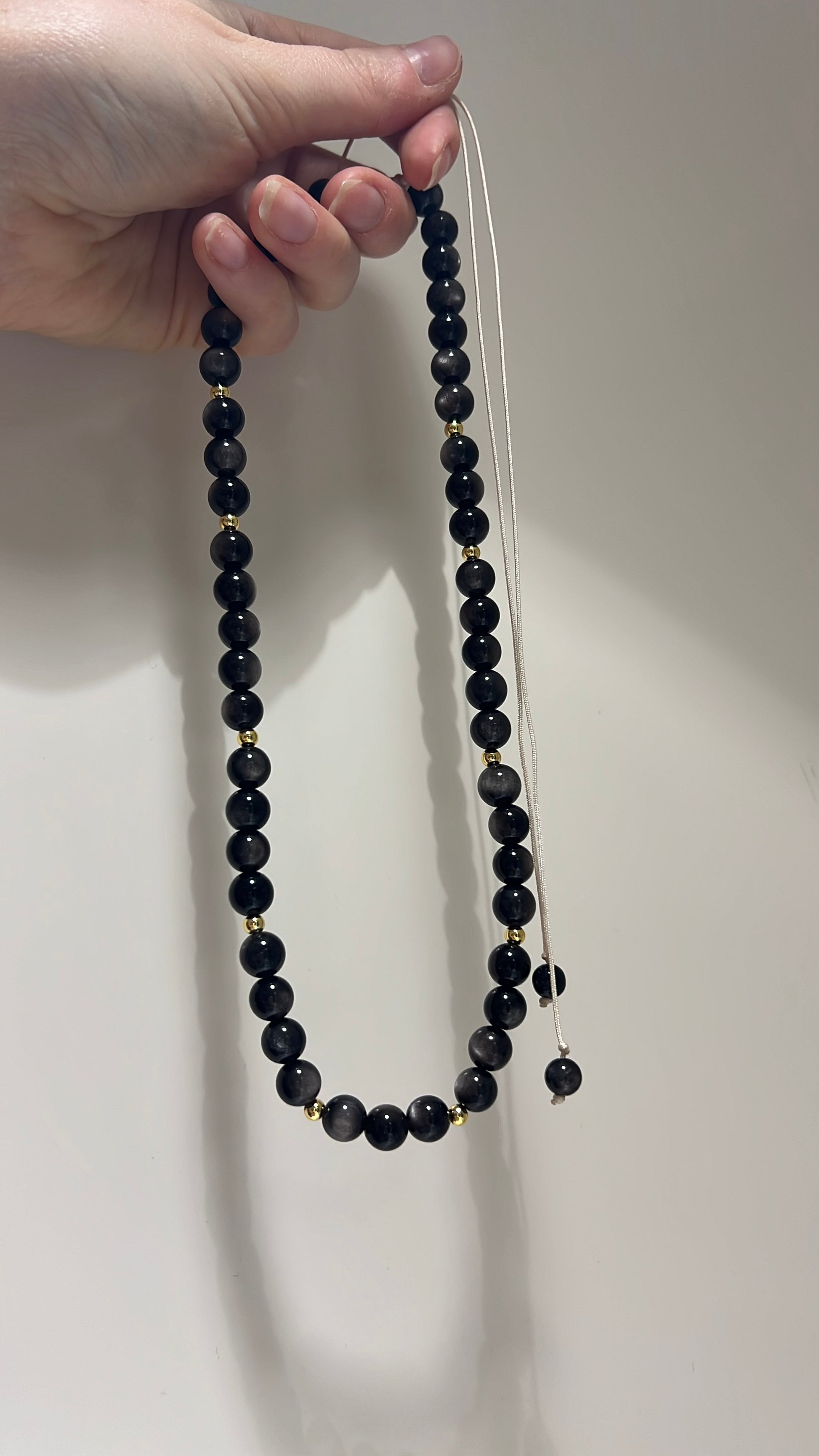Black beaded necklace held by a hand against a plain background