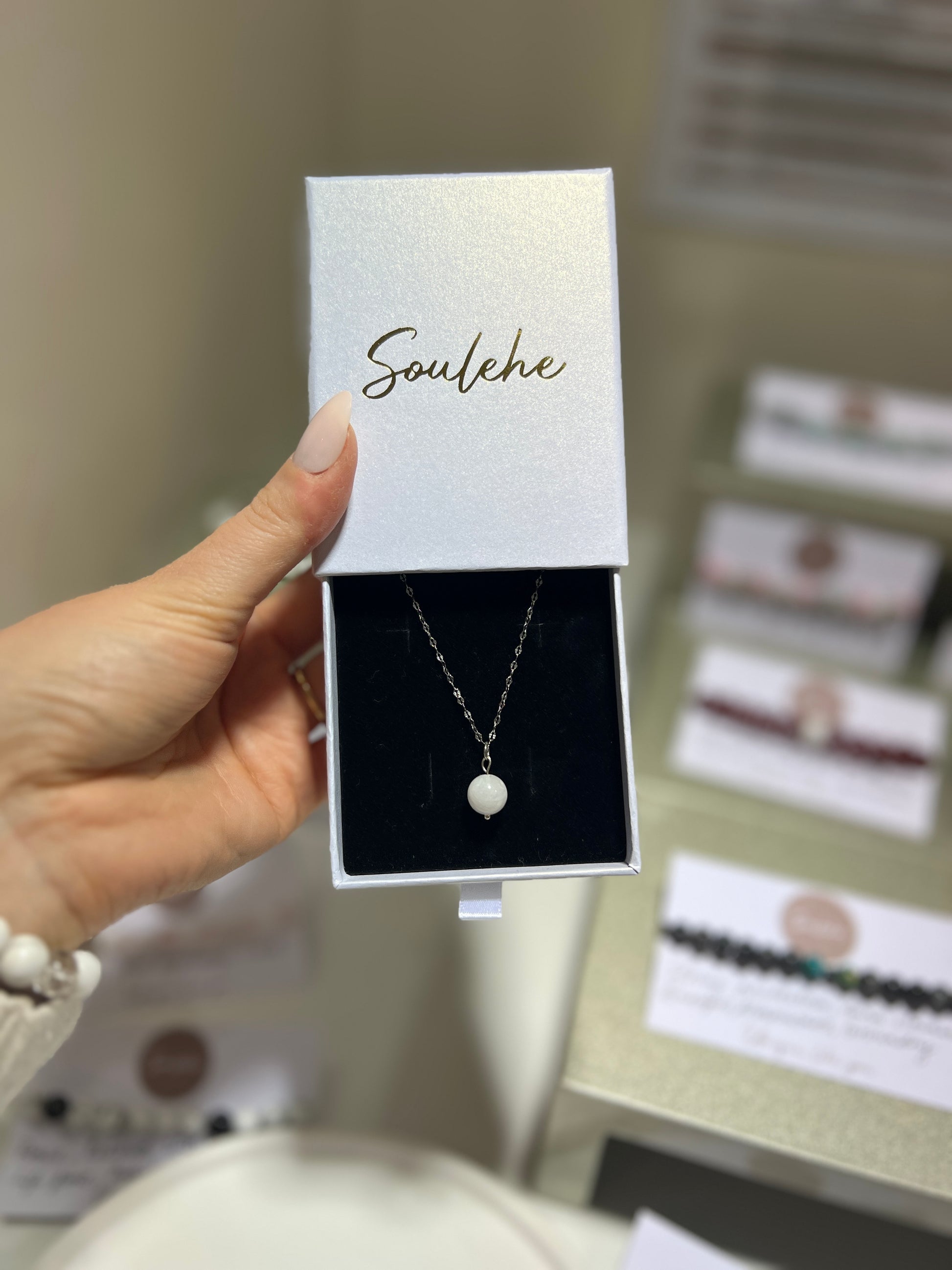 Necklace in a 'Soulehe' box held by a hand with a blurred background