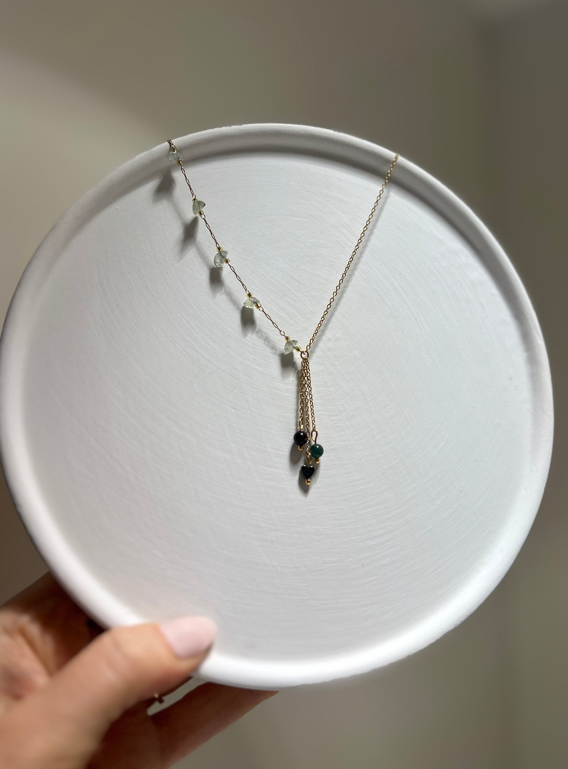 Necklace with a pendant on a white plate held by a hand against a neutral background