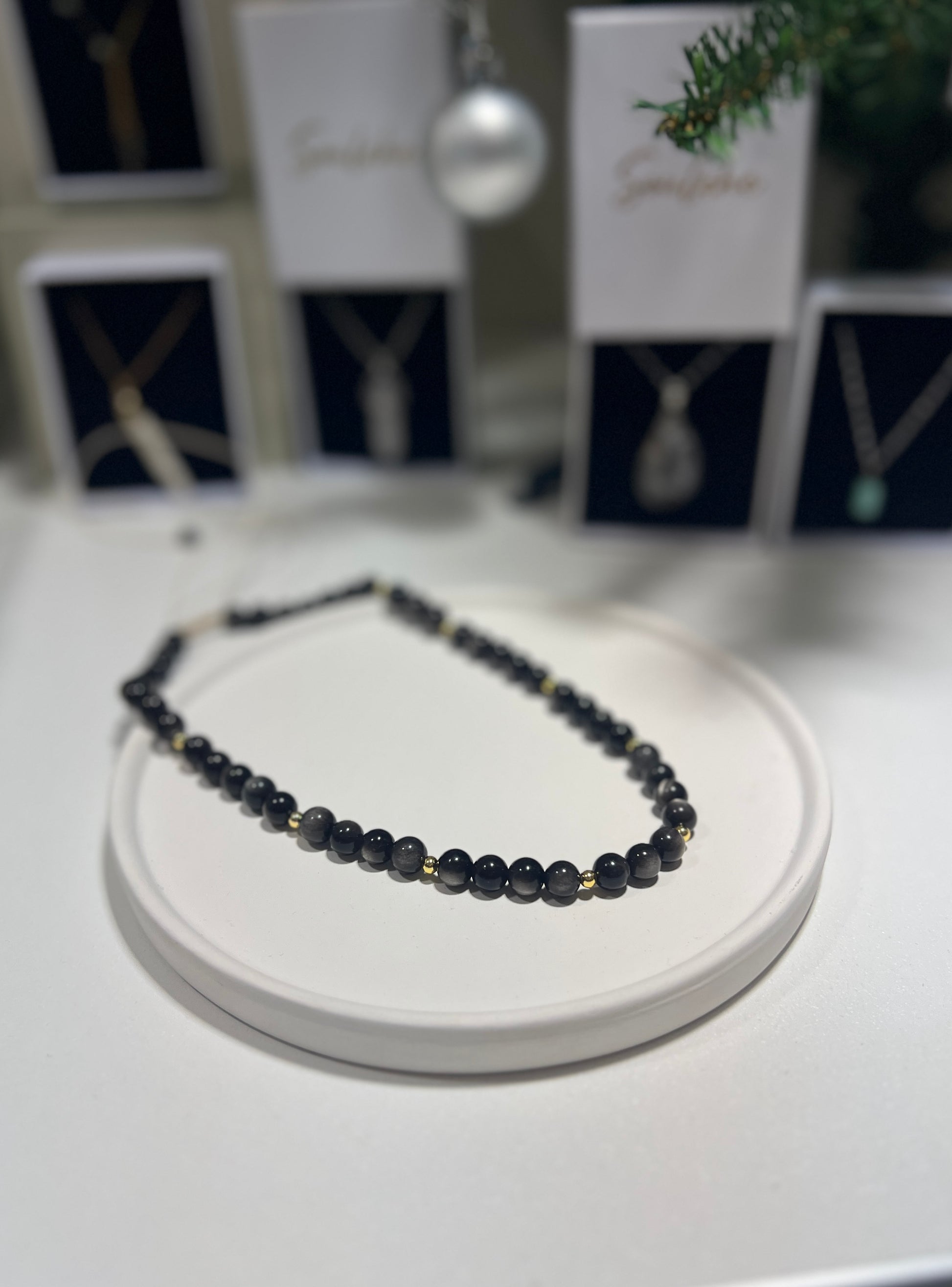 Necklace with dark beads on a white stand with blurred jewelry display in the background