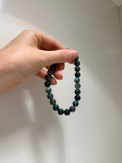 Hand holding a black beaded bracelet against a white background