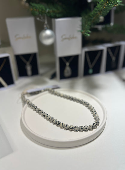 Silver necklace on a white stand with branded packaging in the background