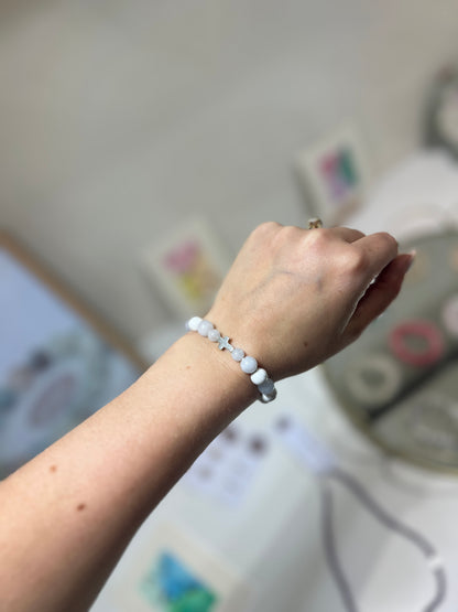 Hand wearing a white beaded bracelet with a blurred background