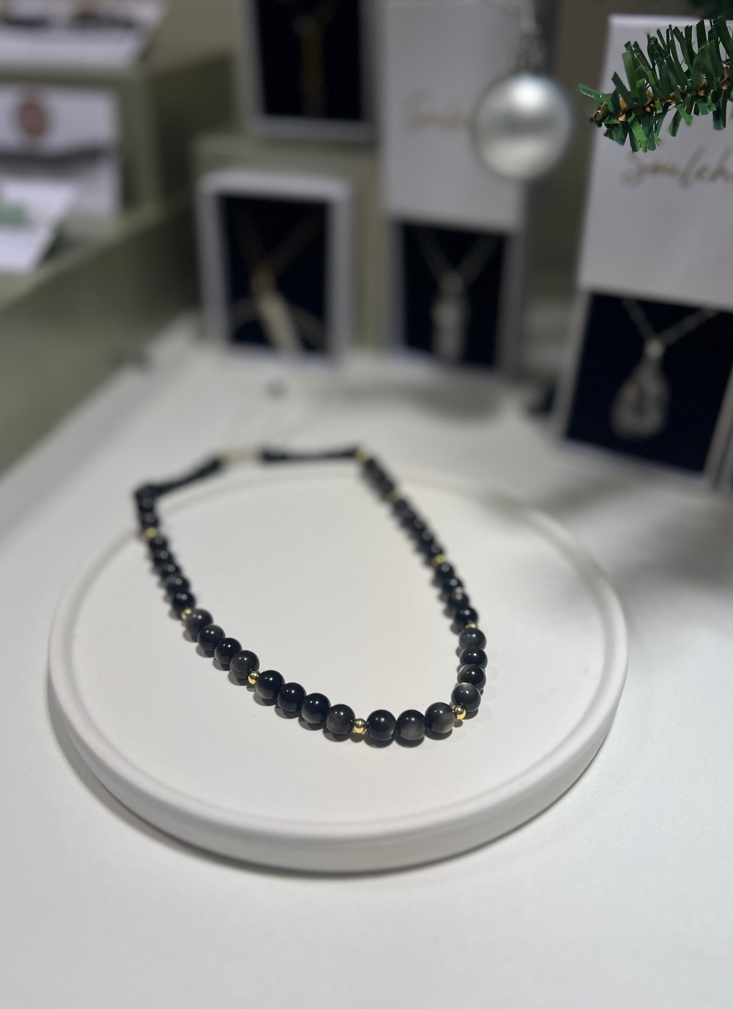 Black beaded necklace on a white stand with blurred jewelry display in the background