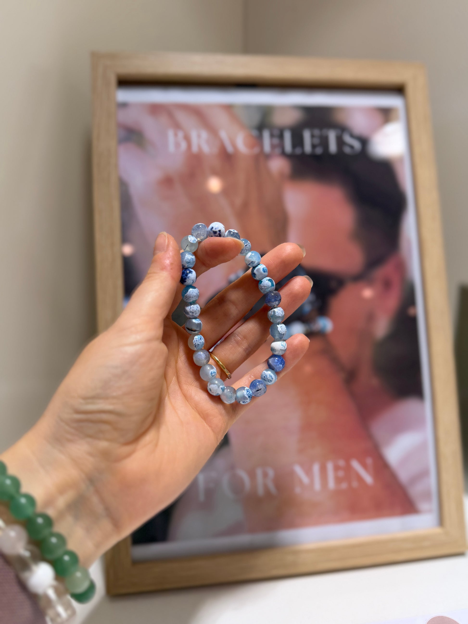 Hand holding a beaded bracelet in front of a magazine with 'Bracelets for Men' on the cover.
