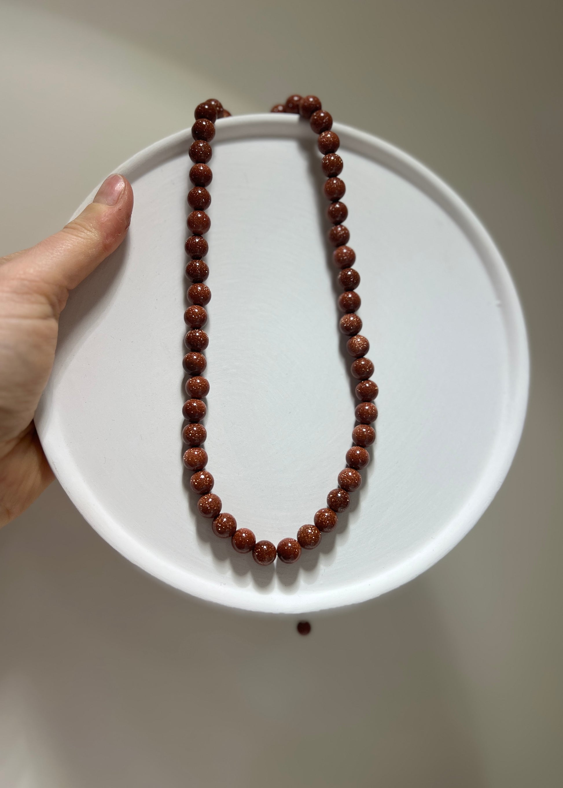 Brown beaded necklace on a white plate held by a hand against a neutral background