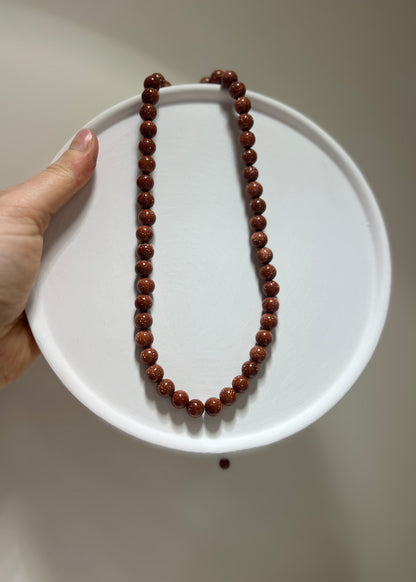 Brown beaded necklace on a white plate held by a hand against a neutral background