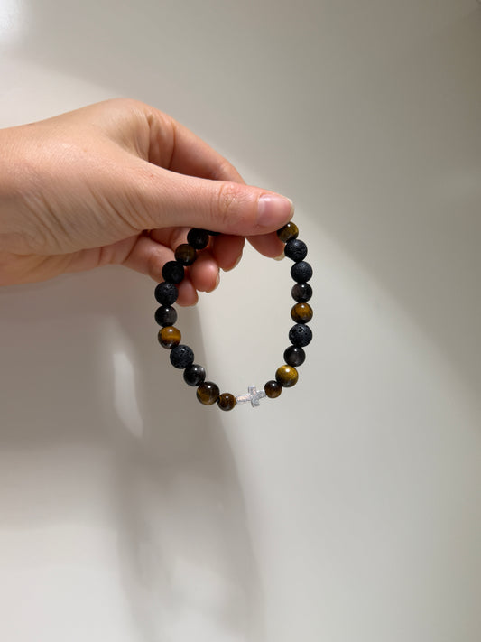 Hand holding a beaded bracelet with a cross charm against a plain background